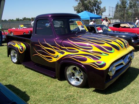 2002 Ford Mustang - Customized purple 1956 Ford F-100 pickup truck with vibrant flame graphics is displayed on a grassy field.