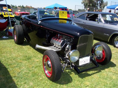 2002 Ford Mustang - A black convertible hot rod with a prominent engine is displayed on a grassy field next to other vehicles.