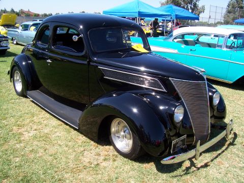 2002 Ford Mustang - A black 1937 Ford Coupe is parked on grass at an outdoor car show with other vehicles present.