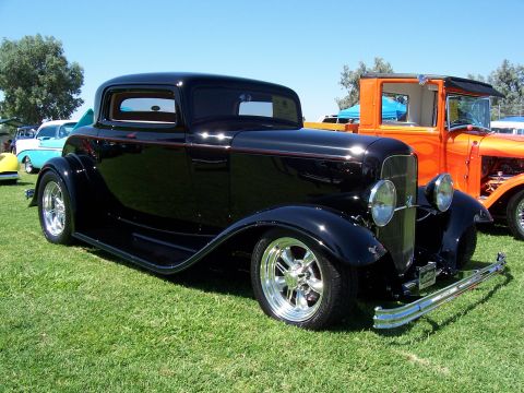 2002 Ford Mustang - A classic black coupe with chrome wheels sits on a grassy field next to an orange truck.