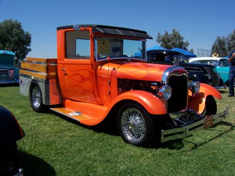 2002 Ford Mustang - An orange hot rod pickup truck with flame decals is parked on a grassy field with other vehicles in the background.