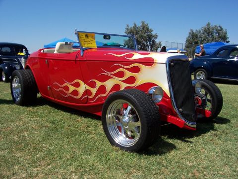 2002 Ford Mustang - A custom hot rod with flame graphics is displayed on a grassy field with other vehicles in the background.
