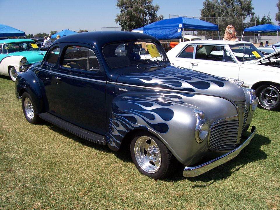 Dark blue coupe with silver flame graphics, chrome bumper, and custom wheels parked on grass