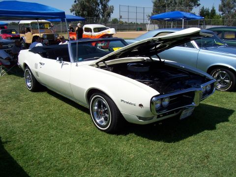 2002 Ford Mustang - White convertible parked on grass with hood open, other vehicles and tents in background.