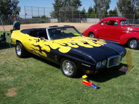 2002 Ford Mustang - Customized black and yellow convertible with flame graphics parked on grass next to a red coupe.