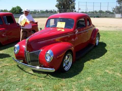 2002 Ford Mustang - A man stands next to a red hot rod coupe, with another red vehicle visible to the left.