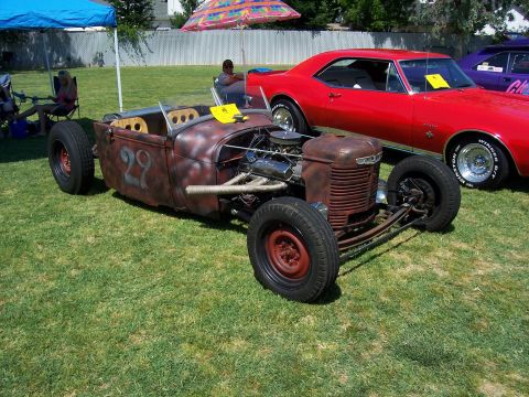 2002 Ford Mustang - A custom-built rat rod sits on grass next to a red muscle car under a blue tent.