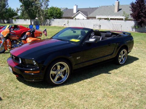 2002 Ford Mustang - A black convertible GT Mustang with red racing stripes is parked on a grassy lawn next to a motorcycle.