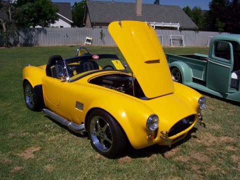 2002 Ford Mustang - A yellow convertible sports car is displayed outdoors with its hood open, parked next to a teal pickup truck.
