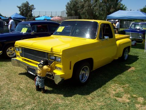 2002 Ford Mustang - A bright yellow pickup truck is parked on a grassy field, with a child examining its front bumper. Another vehicle is visible behind it.