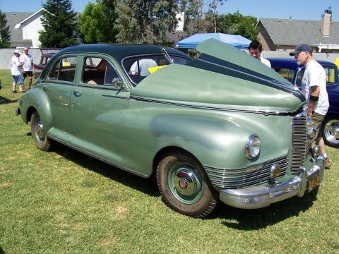 2002 Ford Mustang - A classic green sedan is displayed with its hood open, revealing the engine compartment to onlookers.