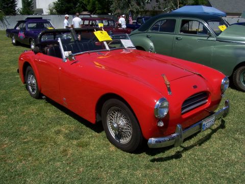 2002 Ford Mustang - A red convertible sports car is parked on a grassy field with other vehicles in the background.