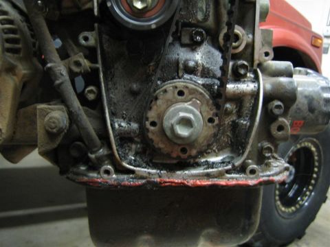 1987 Suzuki Samurai - Close-up of a dirty engine timing belt and gears, with a red vehicle in the background.