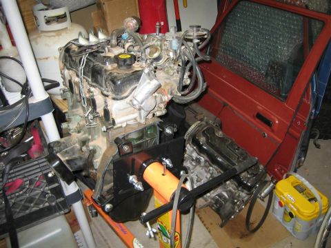 1987 Suzuki Samurai - Engine on an engine stand, next to a red vehicle door. The engine appears to be disassembled.