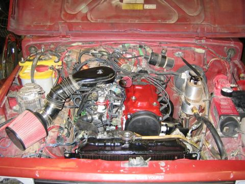 1987 Suzuki Samurai - The engine bay of a red Suzuki Samurai shows its mechanical components and wiring, with an aftermarket air filter installed.