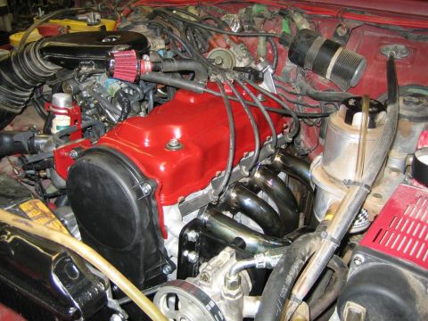 1987 Suzuki Samurai - Close-up of an engine bay with custom modifications including a red valve cover and exhaust headers.