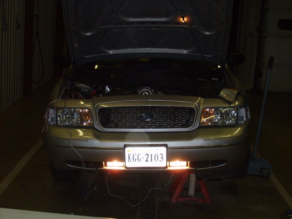 Gold Ford Crown Victoria with hood open, front view. Aftermarket lights installed below license plate