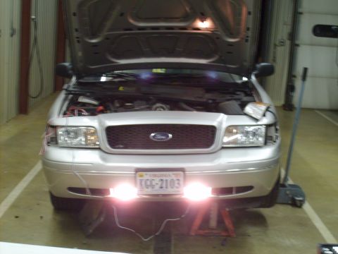 2004 Ford Crown Victoria - Front view of a white Ford Crown Victoria in a shop with the hood up and the front end on jack stands, showing newly installed driver-side…