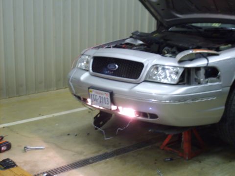 2004 Ford Crown Victoria - Front three-quarter view of a silver Ford Crown Victoria sedan with the hood open, front end partially disassembled, and aftermarket lights…