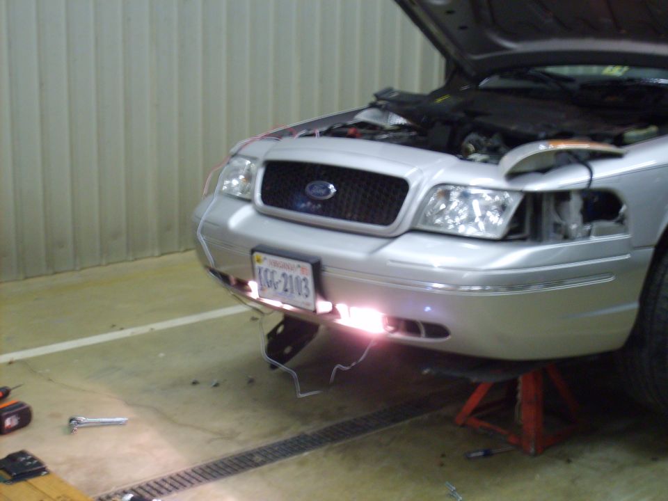 Silver Ford Crown Victoria with open hood and lit lower lights in a garage
