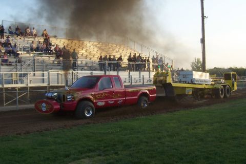 1994 Ford F-150 - A modified red pickup truck is competing in a pull event, generating significant exhaust smoke.