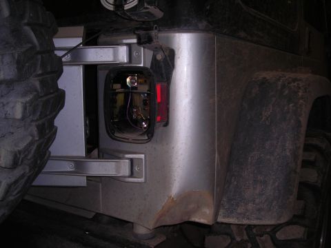 2003 Jeep TJ - The rear corner of a silver Jeep Wrangler shows a removed taillight assembly and a portion of the spare tire.