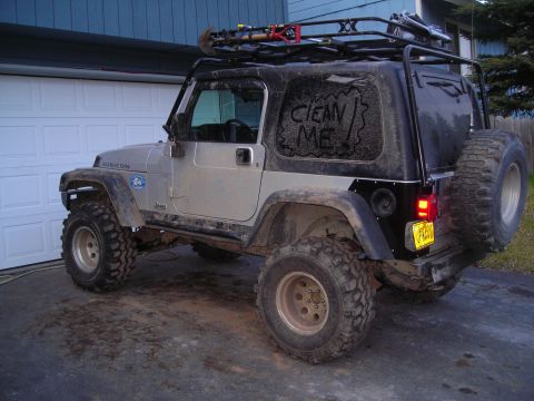 2003 Jeep TJ - A dirty Jeep Wrangler is parked in front of a garage door, with tools on its roof rack.