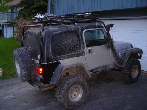 2003 Jeep TJ - A silver and black Jeep TJ is parked in front of a garage, equipped with a roof rack and snorkel.