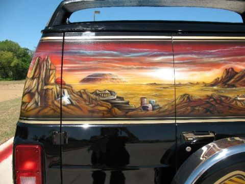 1978 Ford E250 - A van's rear quarter panel displays a vibrant desert sunset mural with rocky formations and alien-like structures.