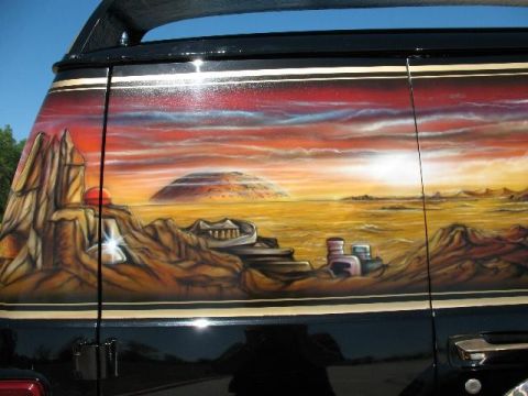 1978 Ford E250 - Custom airbrushed mural adorns the side of a black van, depicting a surreal desert landscape under a vibrant sunset.