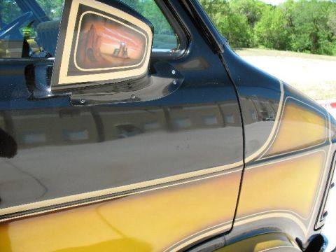 1978 Ford E250 - The side mirror of a van features custom airbrushed artwork of a desert scene with a sunset.