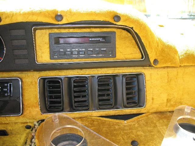 Dashboard of a van with yellow fuzzy upholstery, an aftermarket radio, and air vents