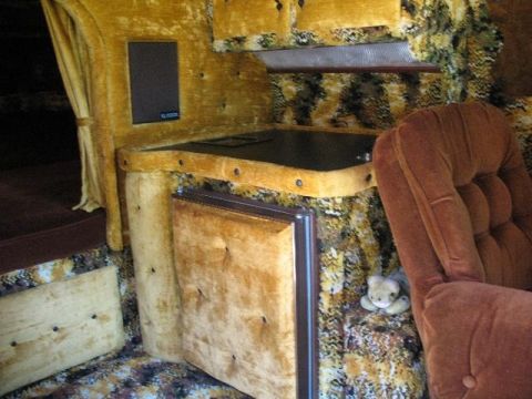 1978 Ford E250 - The interior of a van features a custom build with velvet upholstery and a small kitchenette area.
