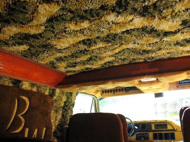Interior of a van with shag carpet on the ceiling and brown seats. A large 'B' is visible on a brown panel