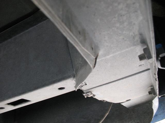 Underside of a vehicle frame with visible rust and damage