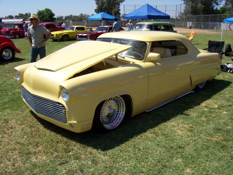 2002 Ford Mustang - Customized yellow coupe on display at an outdoor car show with other vehicles present.