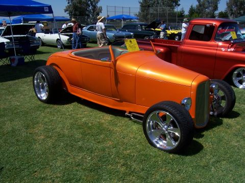2002 Ford Mustang - An orange hot rod is parked on a grassy field next to a red pickup truck and other vehicles.