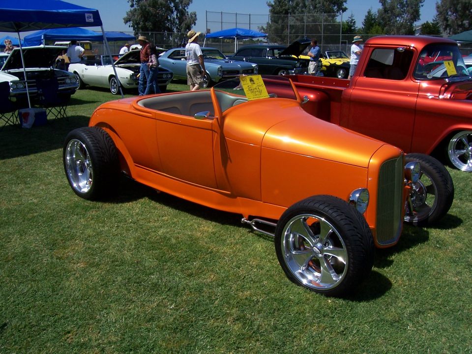 Orange hot rod with chrome wheels and wide tires, parked on grass