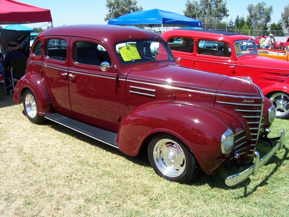 maroon sedan with chrome trim and aftermarket wheels, parked on grass next to a red hot rod