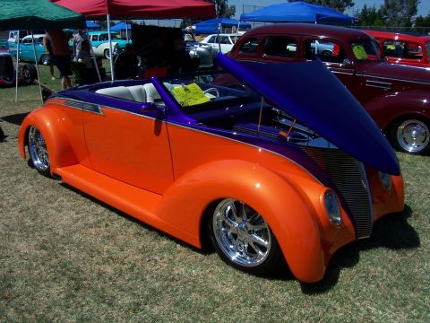 2002 Ford Mustang - A two-tone custom convertible with its hood open is displayed at an outdoor event with other vehicles and tents in the background.