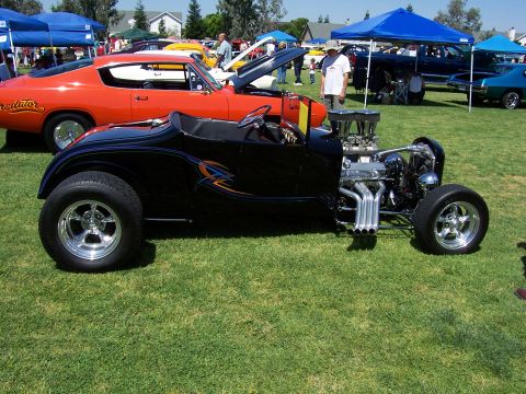 2002 Ford Mustang - A black hot rod with a powerful engine is parked on the grass at an outdoor car show.