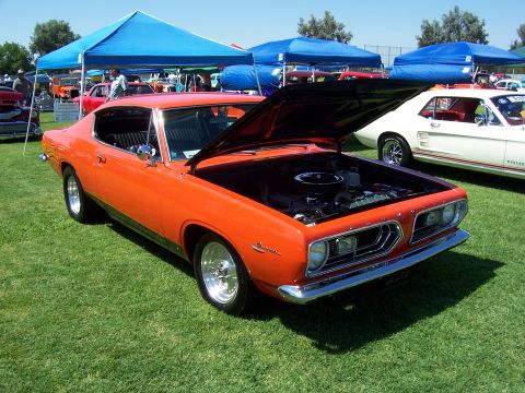 2002 Ford Mustang - An orange 1967 Plymouth Barracuda is displayed with its hood open at an outdoor car show.
