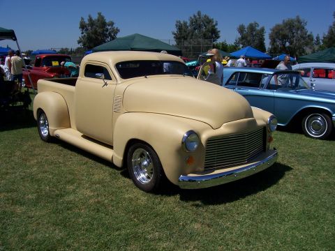 2002 Ford Mustang - A tan pickup truck is parked on grass at an outdoor event with other vehicles and tents in the background.