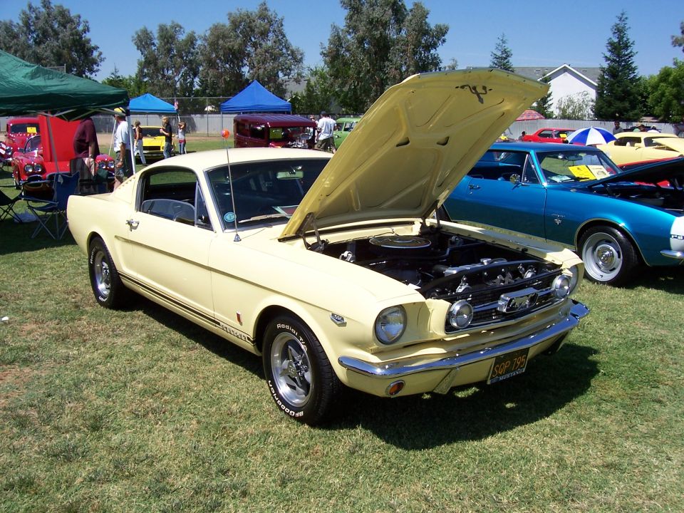 Yellow 1965 Ford Mustang coupe with hood open, parked on grass