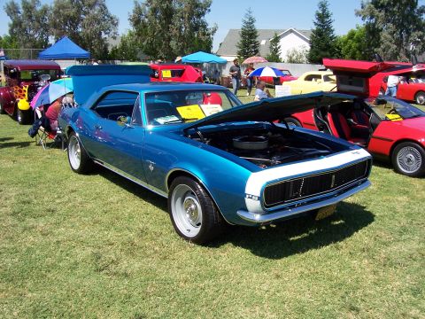 2002 Ford Mustang - A blue 1967 Chevrolet Camaro is displayed with its hood open at an outdoor car show.
