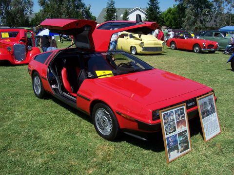 2002 Ford Mustang - A red DeLorean DMC-12 is displayed with its iconic gull-wing doors open at an outdoor car show.