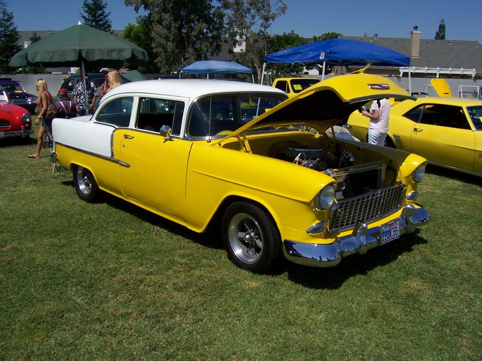 Yellow and white 1955 Chevrolet sedan with hood open, chrome grille, and custom wheels