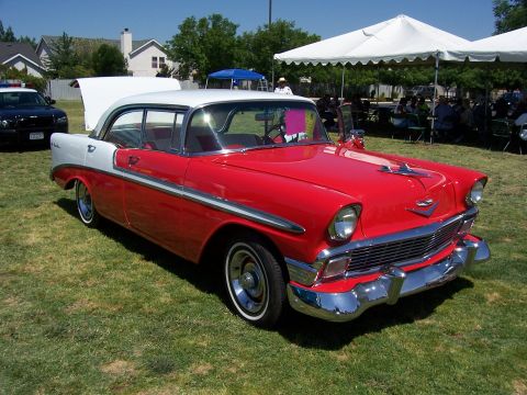 2002 Ford Mustang - A red and white 1956 Chevrolet Bel Air is parked on grass, with a police car visible in the background.