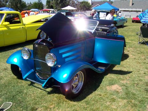 2002 Ford Mustang - A custom blue hot rod is displayed outdoors with its hood open, alongside other vehicles and tents.