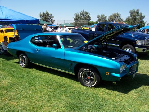 2002 Ford Mustang - A teal classic coupe is displayed with its hood open, alongside a dark blue pickup truck at an outdoor event.